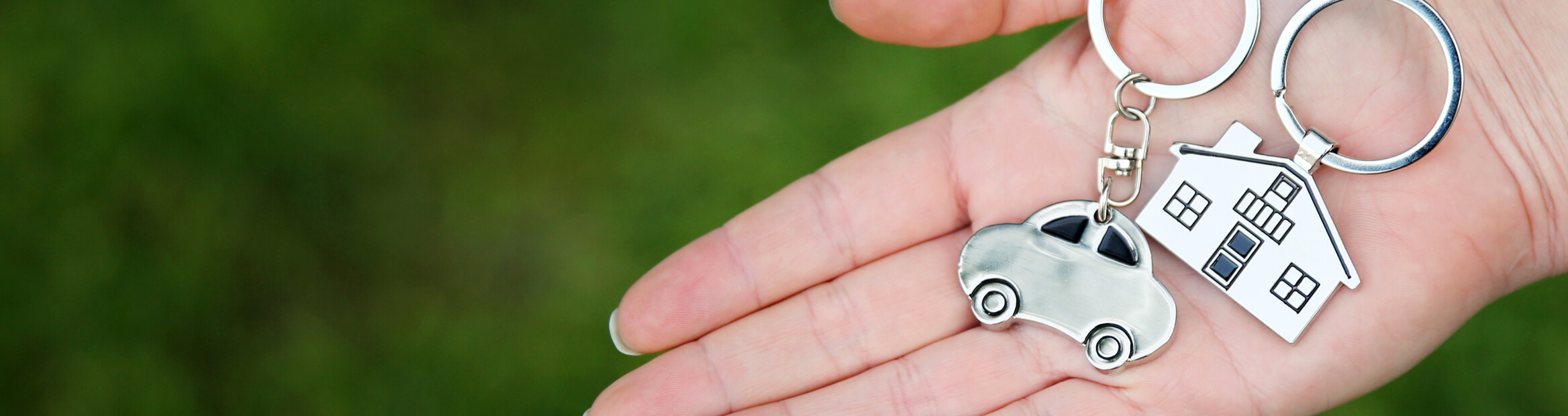 Close-up of a hand holding a car-shaped keychain and a home-shaped keychain