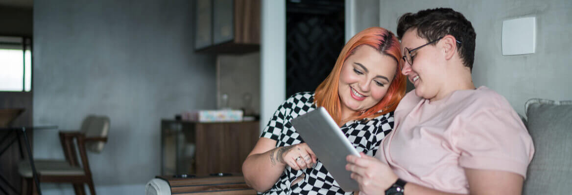 Two roommates sitting on living room couch looking at a computer tablet