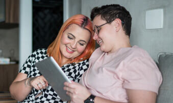 Two roommates sitting on living room couch looking at a computer tablet